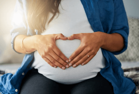 Expecting mother forms a heart on her belly with her hands.